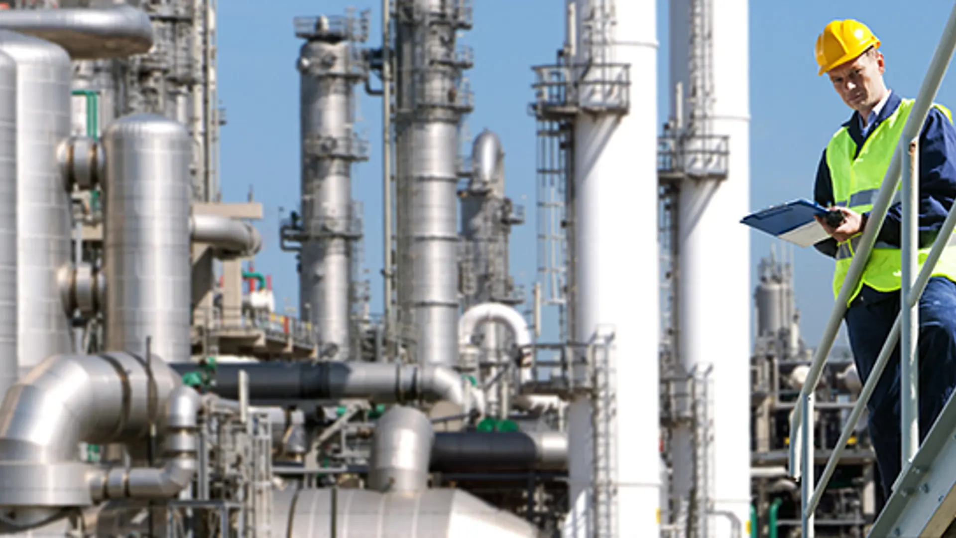Shutterstock _77496391-A Petrochemical Engineer With A Noteboard In His Hand In Front Of A Huge Refinery